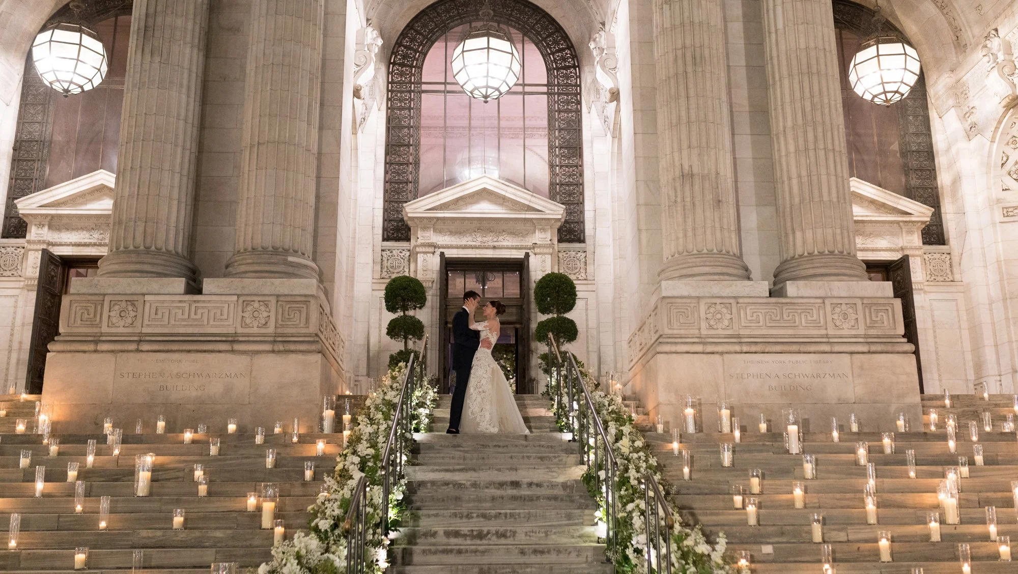 A wedding couple on a candlelit staircase framed by monumental stone columns