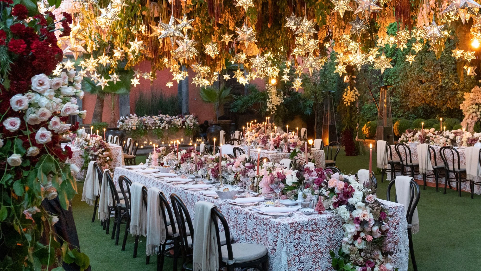 An outdoor dinner with patterned tablecloths, flowers and glowing stars overhead