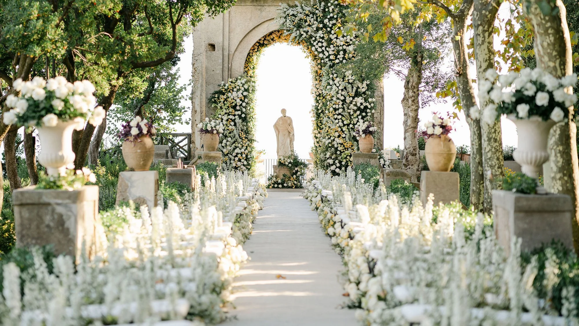 An intimate ceremony with a floral arch and white flowers lining the aisle