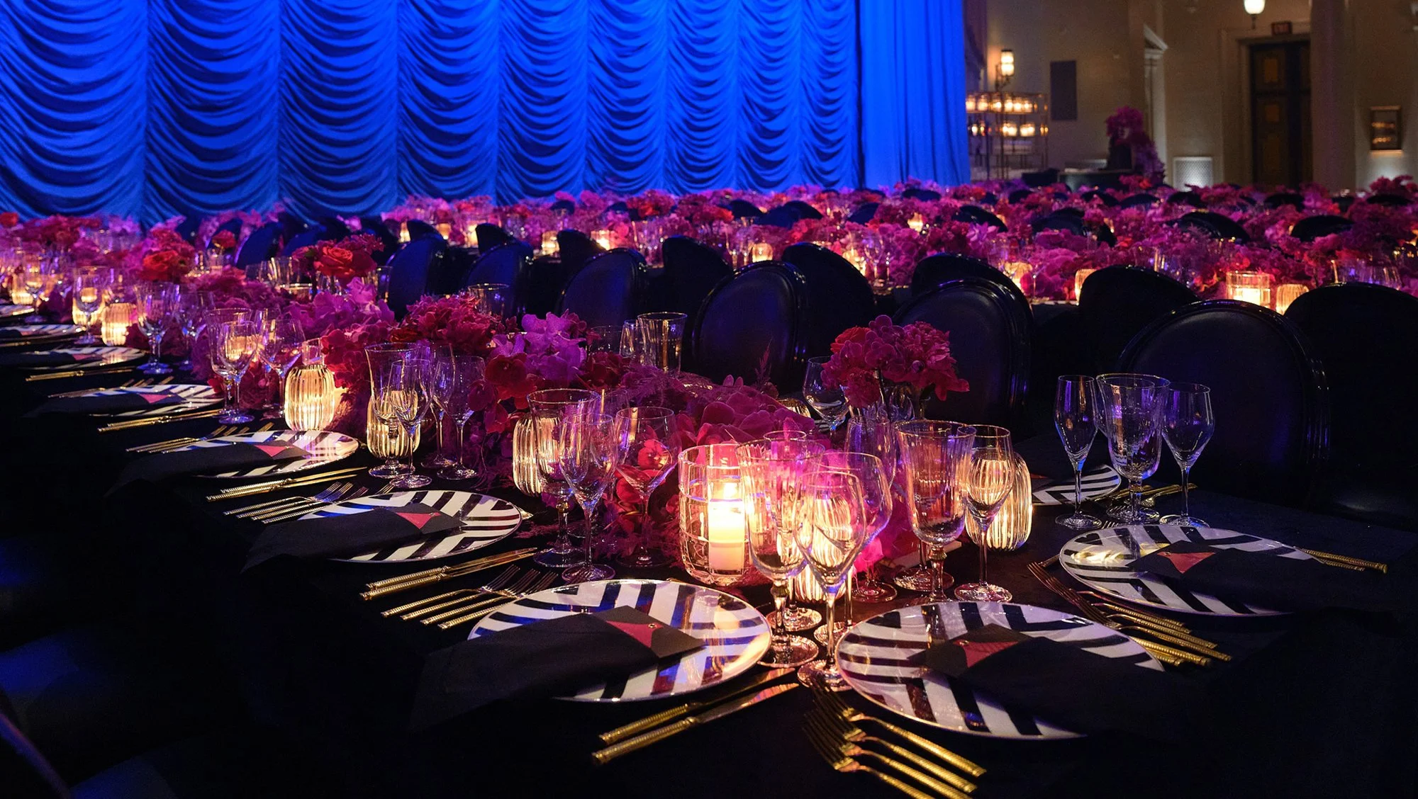 A candlelit celebration with vivid blue draping and magenta floral arrangements